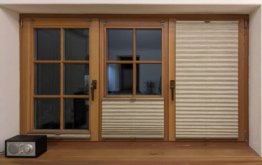Bild eines Fensters mit 3 Fensterflügeln und Sprossen. Auf jedem Fensterflügel ist ein Plissee angebracht. Die Plissees sind in unterschiedlicher Höhe.